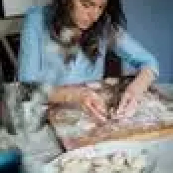 A woman carefully prepares homemade pastries on a wooden board in a cozy kitchen setting.